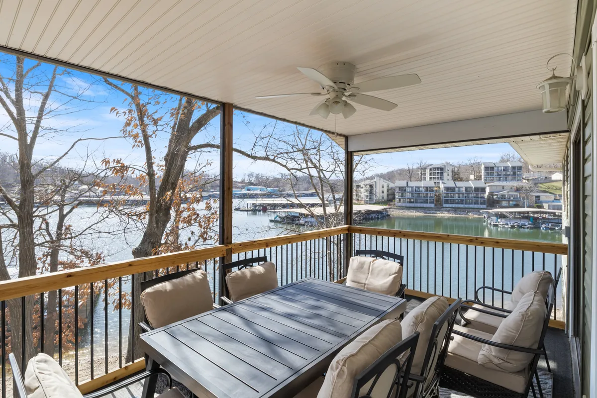 An exterior view of a comfortable outdoor dining area with a table and seating overlooking the waterfront, framed by trees. The space invites relaxation and communal activities in a pet-friendly setting.