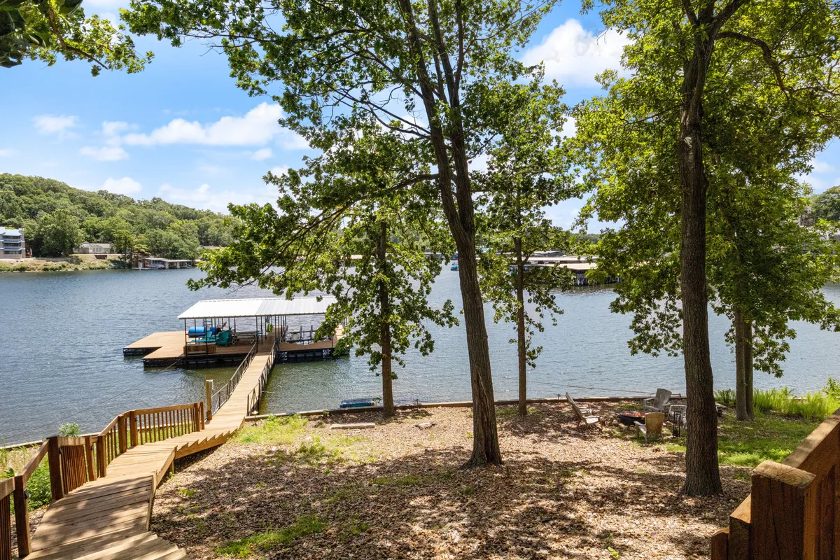 A tranquil exterior view focused on a dock extending into the lake with trees and a gentle pathway leading to the water. The dock appears ready for boating, fishing, or relaxing by the water, with scenic sunset possibilities.