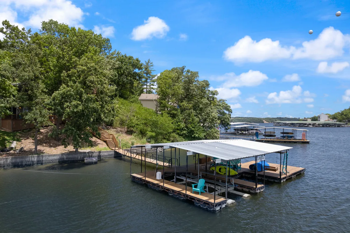 A boathouse sits beside a wooden dock, with kayaks ready for launch and lush greenery surrounding the lake. The inviting scene captures the essence of lakeside adventure, from kayaking and boating to swimming and fishing.