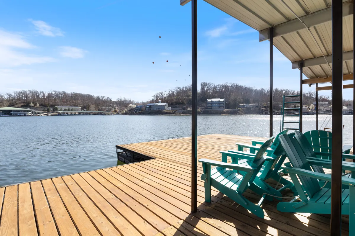 A set of Adirondack chairs is arranged on a dock structure overlooking the water, with the tranquil lake stretching out into the distance. The setting is ideal for sunbathing, relaxing, or stargazing, and demonstrates the inviting nature of the private dock area.