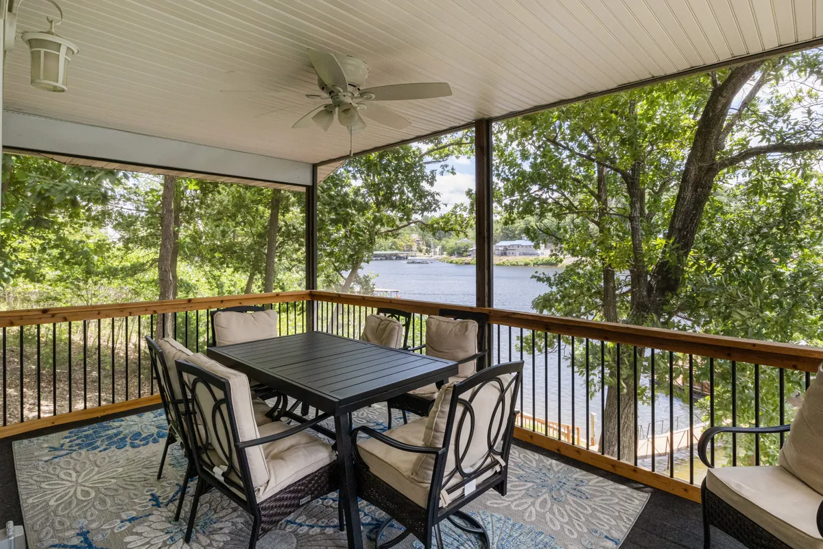 An inviting outdoor dining area set among lush greenery with a water view in the background. A sturdy dining table is surrounded by comfortable chairs, perfect for al fresco meals and social gatherings as the sun sets or rises over the water.