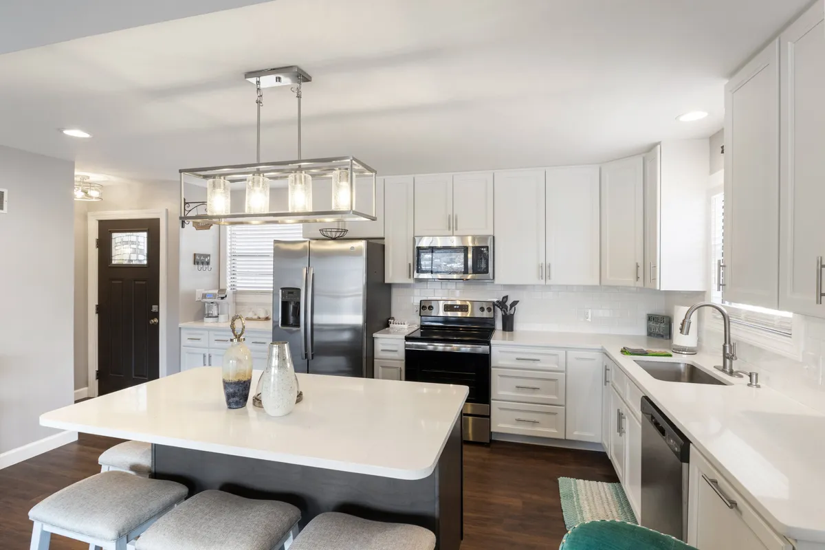 A spacious, modern kitchen featuring a central island countertop, stainless steel appliances, stylish pendant lighting, and ample cabinetry. The island provides plenty of workspace for meal prep and gathering, while the appliances and storage highlight the kitchen's functionality for group cooking.