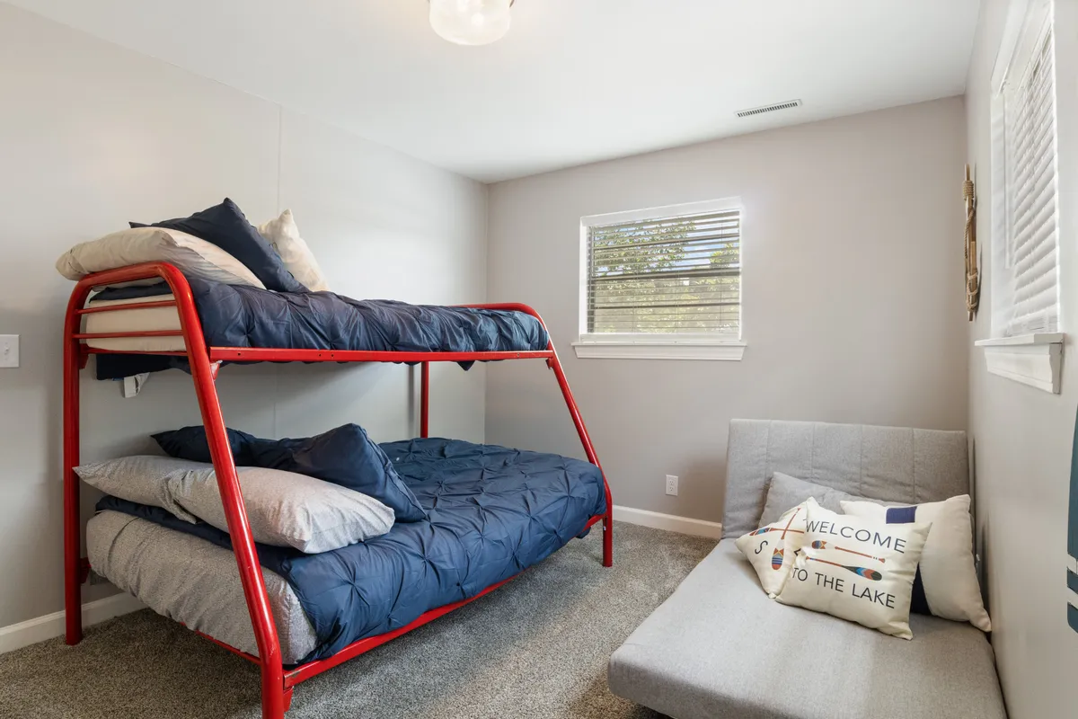 This scene centers on a lower-level bunk room with a bunk bed and a gray sofa, accompanied by playful decorative pillows. The space is designed for comfort and fun, ideal for kids or teens seeking a private retreat after a day by the lake.