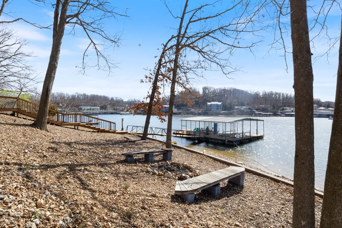 A peaceful lakeside scene featuring the lake, docking area, wooden benches, and surrounding trees. The area is open, serene, and ideal for outdoor recreation such as walks, playing fetch, or simply relaxing by the water.