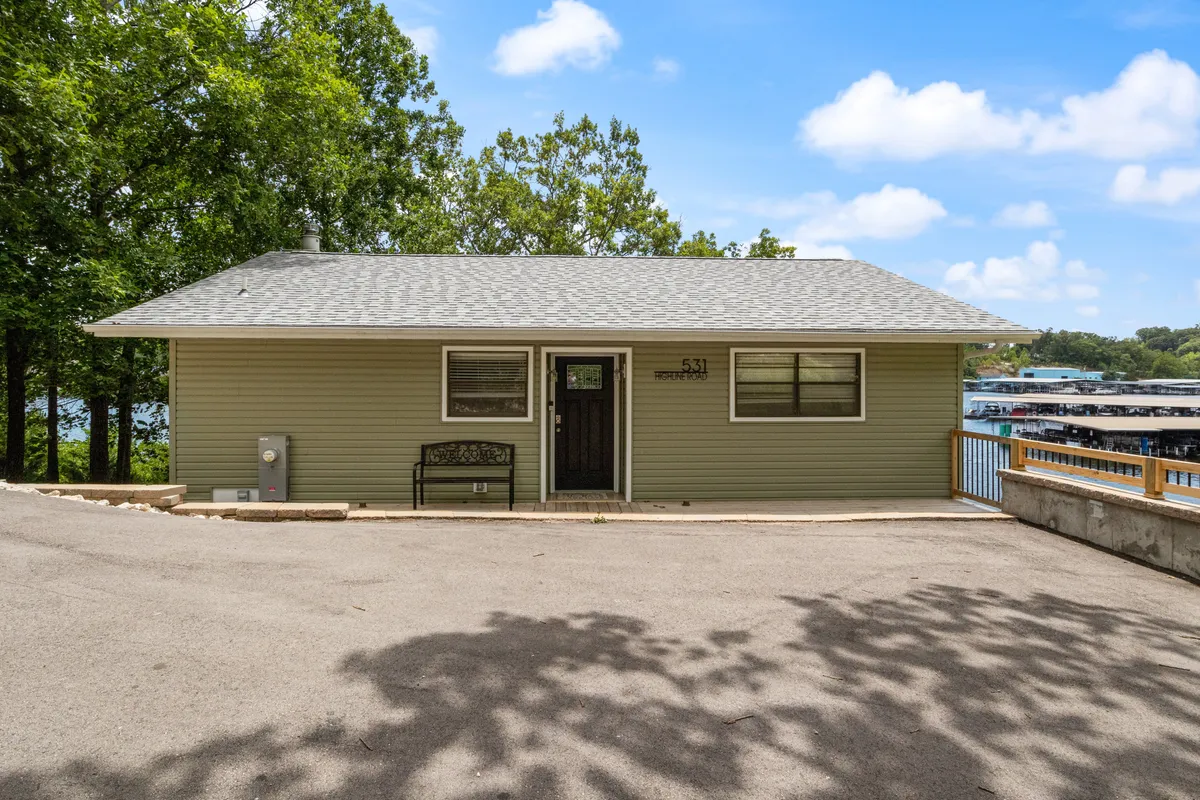 A serene exterior shot showing the house’s front door, outdoor seating, and the dock area, with a view across the water. The image hints at both water activities and the comfort of gathering spaces—front porch, dock, and gentle sunset light.
