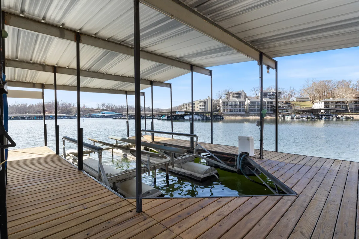 A wooden dock extends over still lake waters, flanked by boat lifts and neighboring buildings along the shoreline. The scene suggests opportunities for boating, fishing, and relaxation right at the water’s edge, with a soft sunrise glow hinting at quiet mornings.