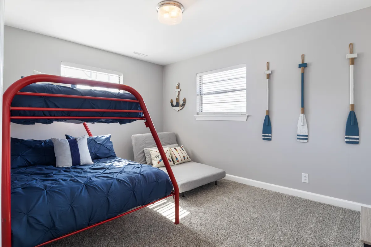 Depicts a cheerful bunk room with a bunk bed, cozy sofa, and playful nautical decor. The space is designed for both sleeping and fun, inviting guests to relax, play games, or enjoy family time.