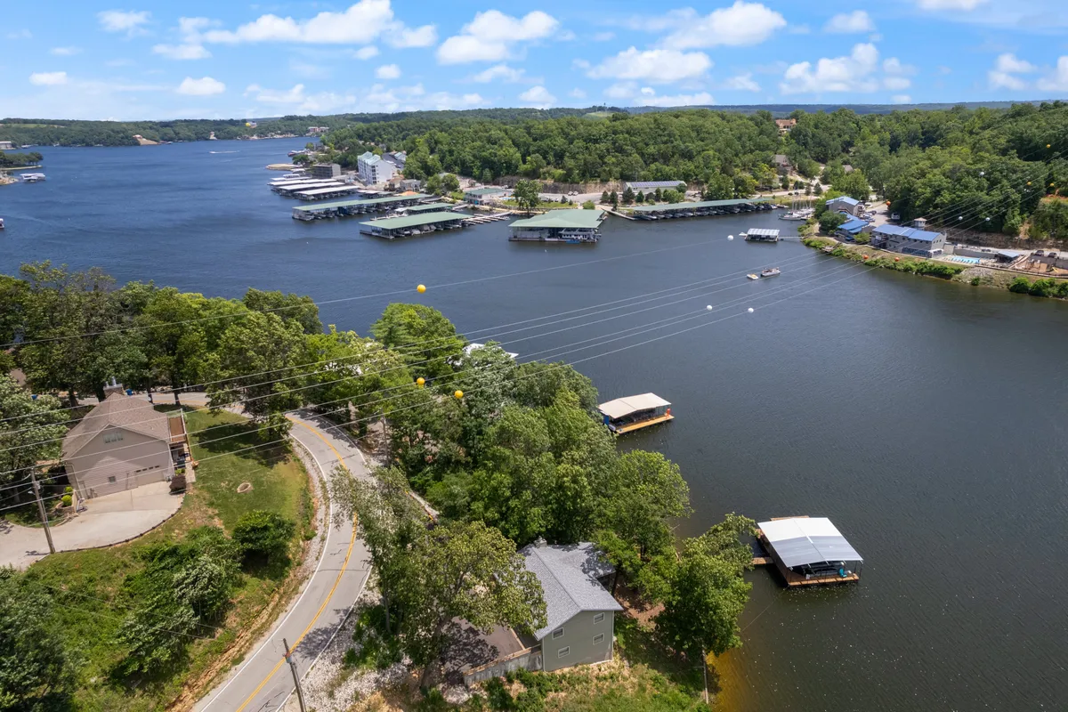 A wide view of the lakefront area, featuring boats on the water, a scenic tree line, and a road leading through lakeside homes. The setting is peaceful and full of potential for exploration, from morning fishing trips to sunset walks along the shore.