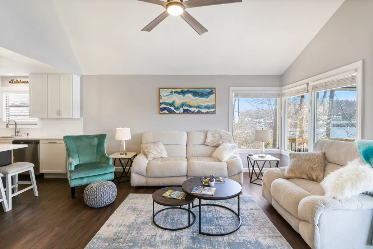 This image showcases a spacious living area with plush sofas, a coffee table, wall art, and expansive windows that provide sweeping views of the lake. The atmosphere is comfortable and welcoming, ideal for relaxing, socializing, and enjoying the stunning natural vistas.